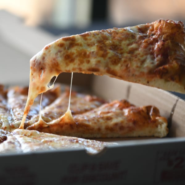 A cheesy slice of Louie's Pizza being lifted from a pizza box, with cheese stretching.