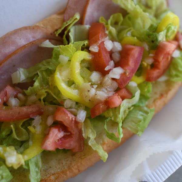 Close-up of a Louie's Pizza sub sandwich with ham, lettuce, tomatoes, onions, and peppers.
