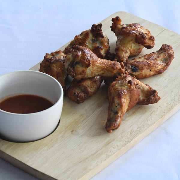 Louie's Pizza chicken wings, golden brown, on a wooden board with a side of dipping sauce.