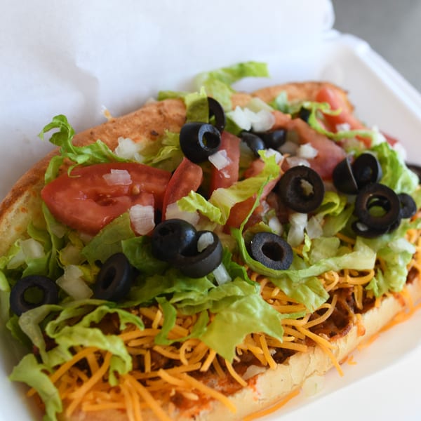 Louie's Pizza taco sub with shredded cheese, lettuce, tomatoes, onions, and black olives.