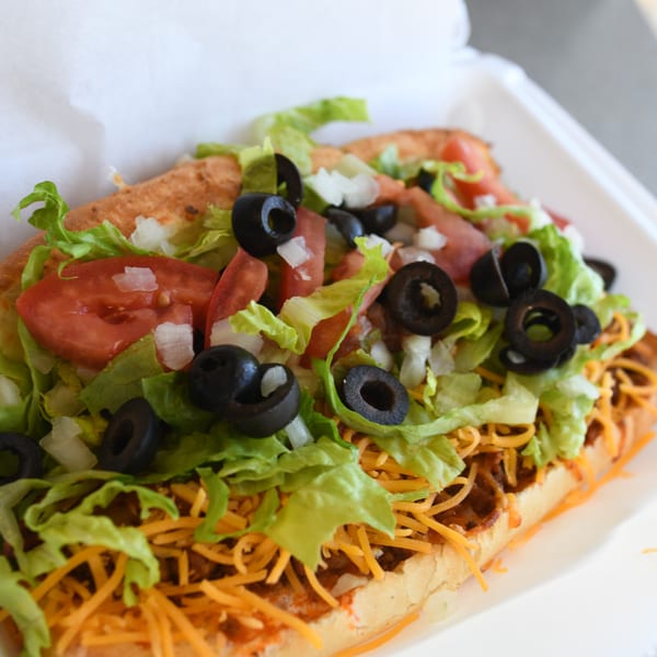 Louie's Pizza taco sub with shredded cheese, ground beef, lettuce, tomatoes, onions, and black olives.