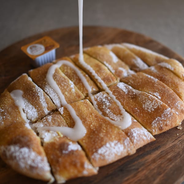 Sweet cinnamon sticks from Louie's Pizza, drizzled with white icing and powdered sugar.