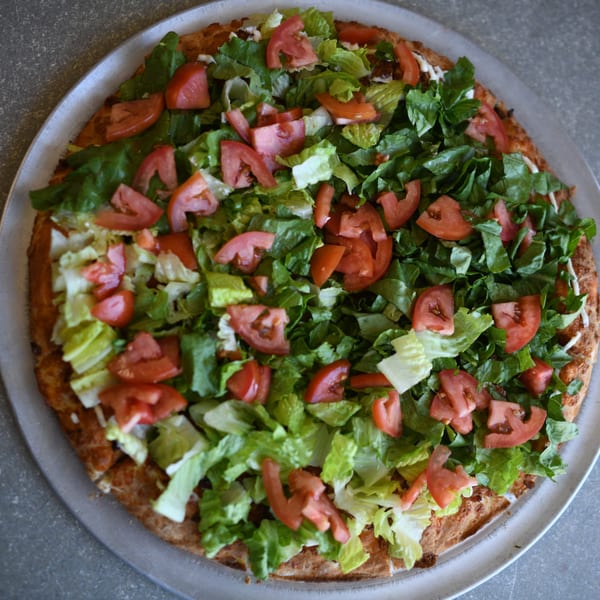 Louie's Pizza's taco pizza, topped with fresh lettuce and diced tomatoes on a metal tray.