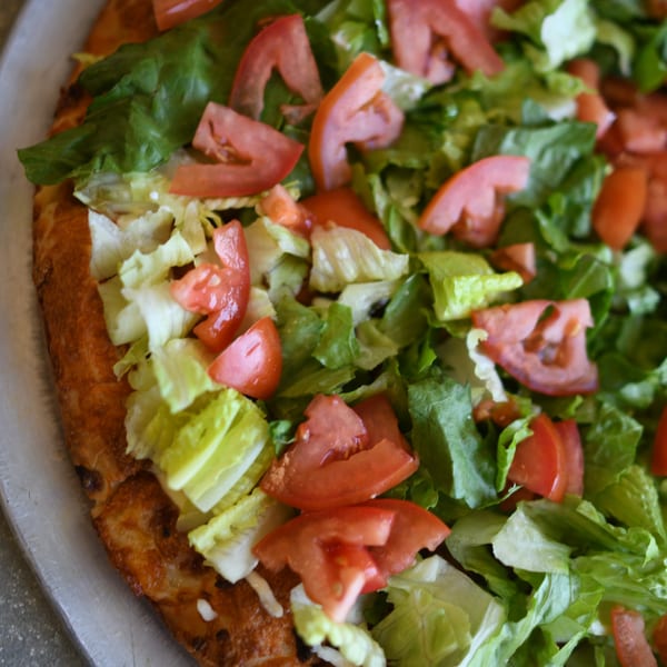Close-up of a Louie's Pizza pizza topped with fresh green lettuce and diced red tomatoes.