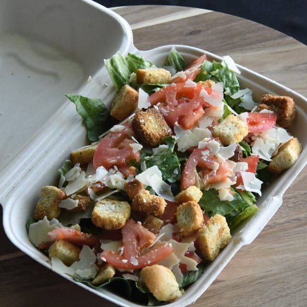 Louie's Pizza Caesar salad with lettuce, tomatoes, croutons, and parmesan cheese in a takeout container.
