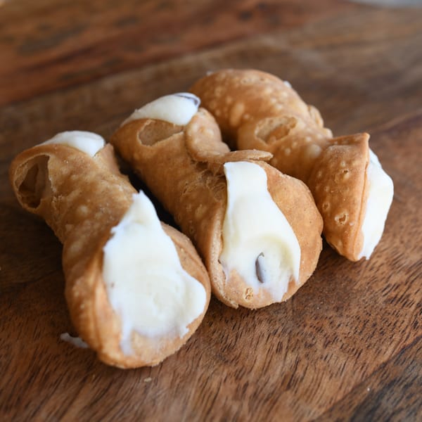 Four Louie's Pizza cannolis, golden-brown shells filled with white cream, on a rustic wooden surface.