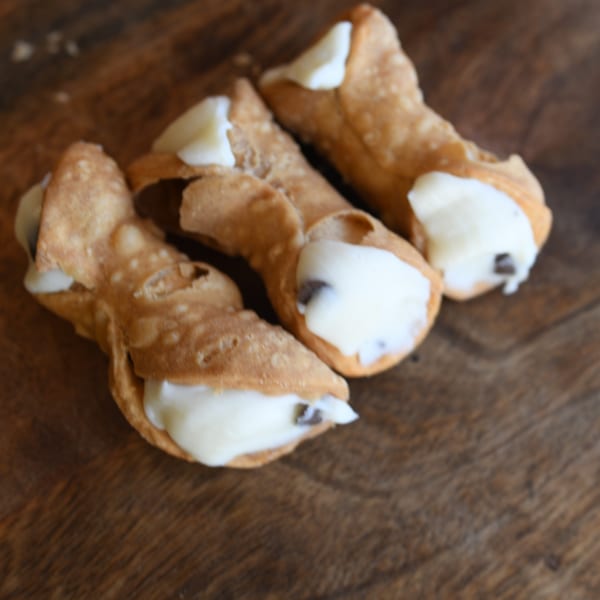 Three Louie's Pizza cannolis filled with white cream and chocolate chips on a wooden surface.