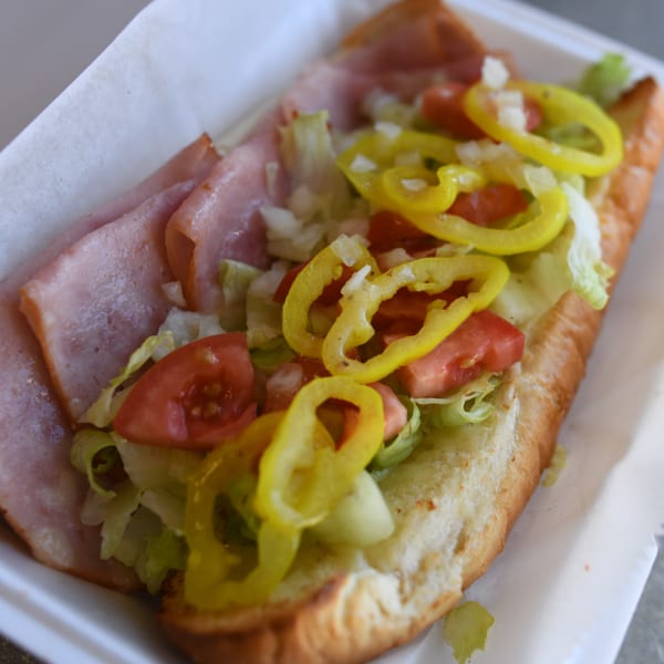 A Louie's Pizza ham sub with lettuce, tomatoes, onions, and banana peppers in a white container.