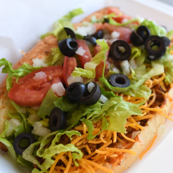 Louie's Pizza taco sub with lettuce, tomatoes, black olives, and shredded cheese.