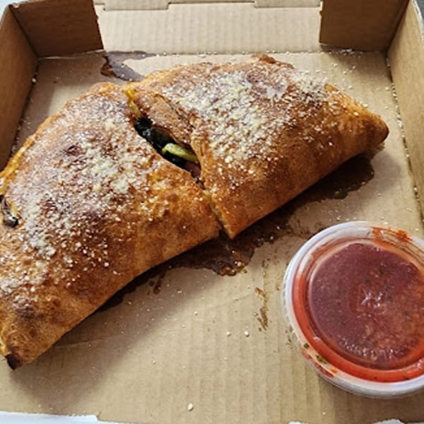 Two golden-brown calzones, dusted with parmesan cheese, in a Louie's Pizza box with a side of marinara.