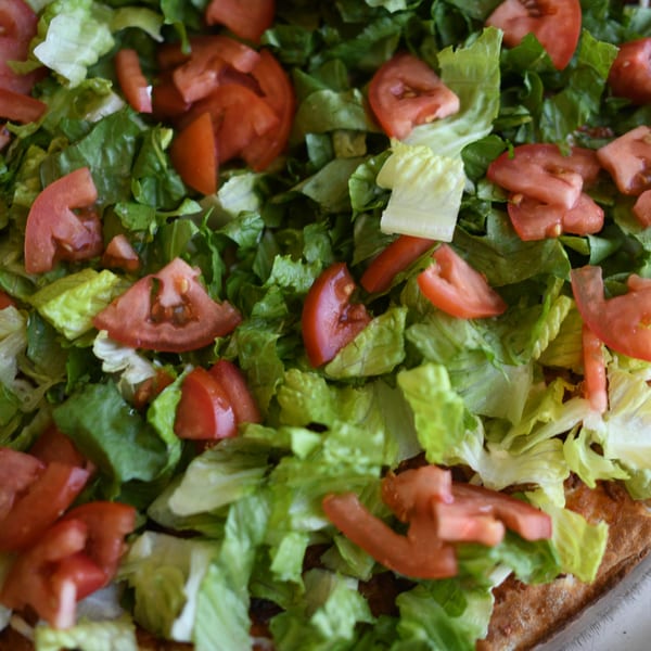 Close-up of a Louie's Pizza taco pizza topped with fresh shredded lettuce and diced tomatoes.