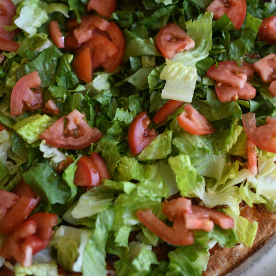 Close-up of a Louie's Pizza taco pizza topped with fresh shredded lettuce and diced tomatoes.