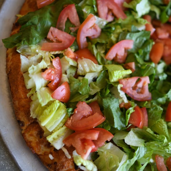 Close-up of a Louie's Pizza pizza topped with fresh green lettuce and sliced red tomatoes.