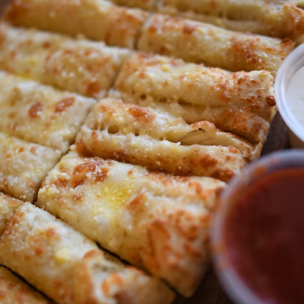 Close-up of Louie's Pizza cheese breadsticks with marinara and ranch dipping sauces.