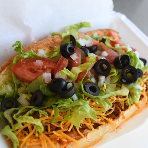 Louie's Pizza taco sub with lettuce, tomatoes, black olives, onions, and shredded cheese.