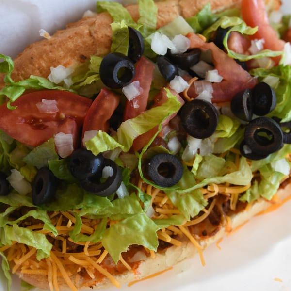 Close-up of a Louie's Pizza sub sandwich with lettuce, tomatoes, black olives, onions, and cheese.