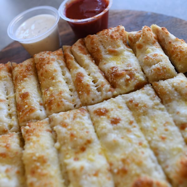 Louie's Pizza cheese breadsticks, golden brown with melted cheese, served with marinara and ranch dipping sauces.