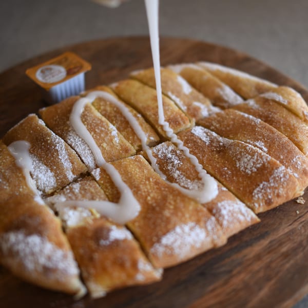 Sweet dessert pizza strips with powdered sugar and white icing drizzled on a wooden board.