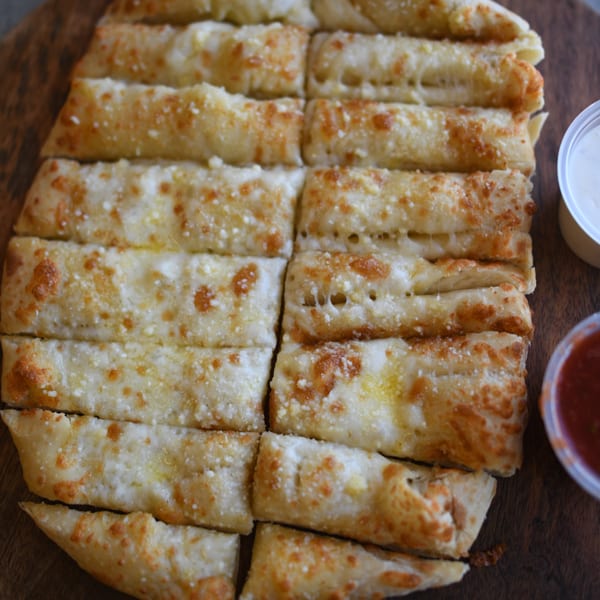 Louie's Pizza garlic breadsticks, golden brown with melted cheese, served with dipping sauces.