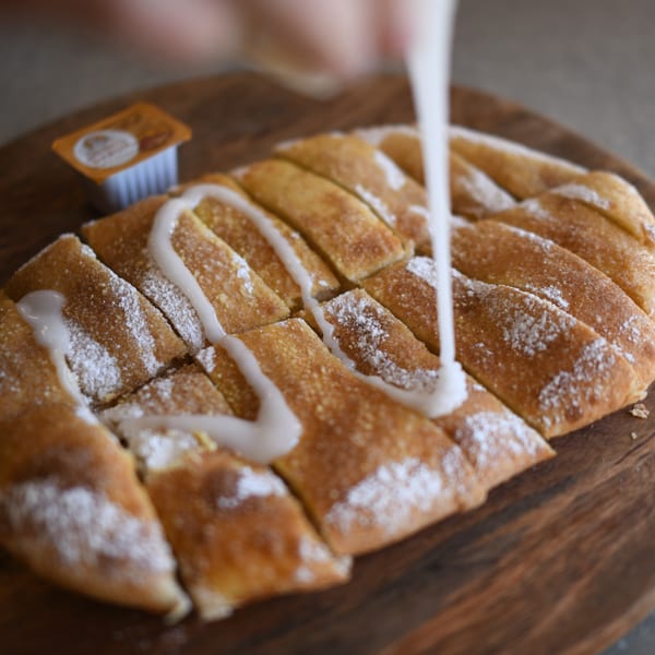 Louie's Pizza cinnamon sticks, dusted with powdered sugar and drizzled with white icing.